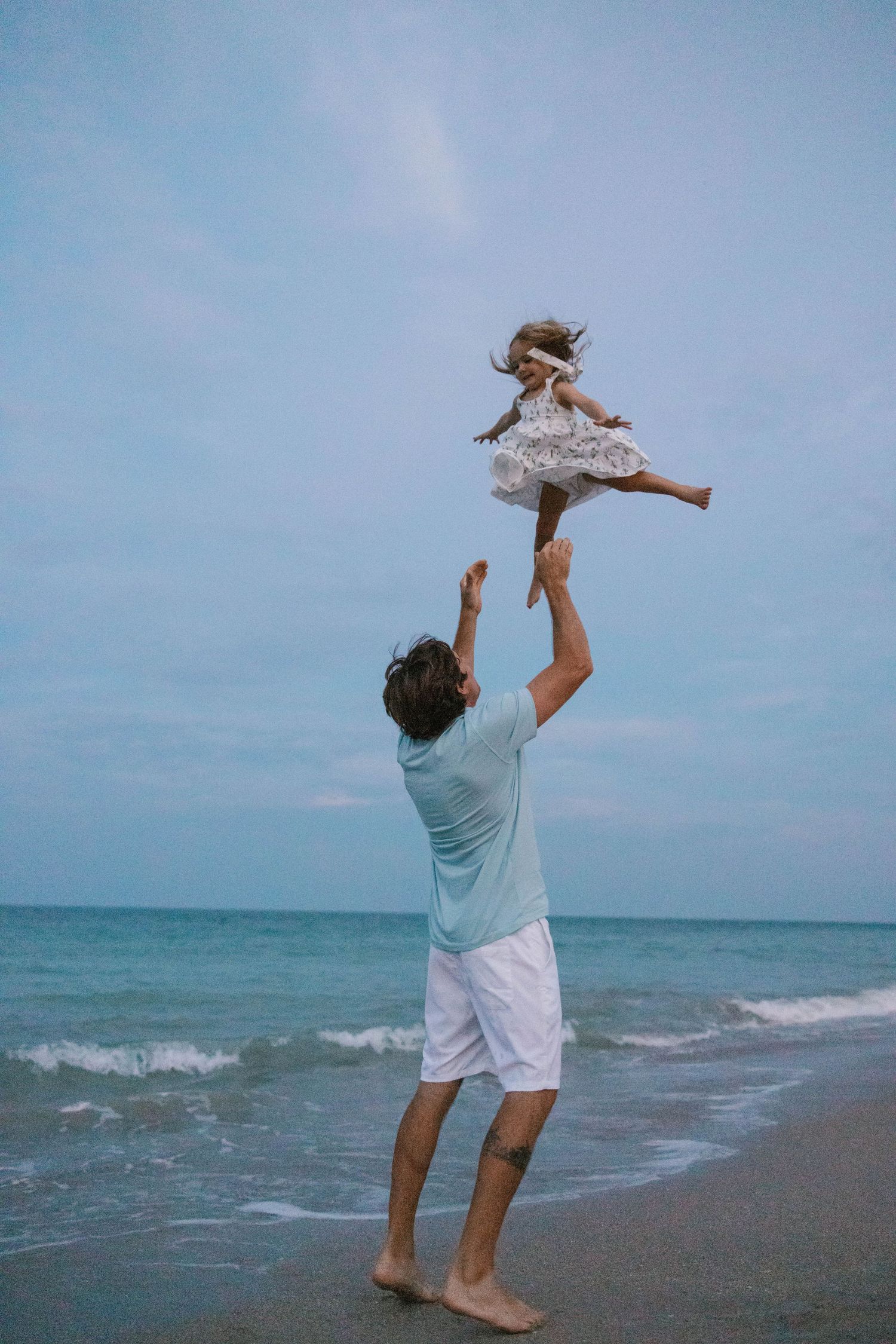 A father joyfully tossing his young daughter into the air on a beach.