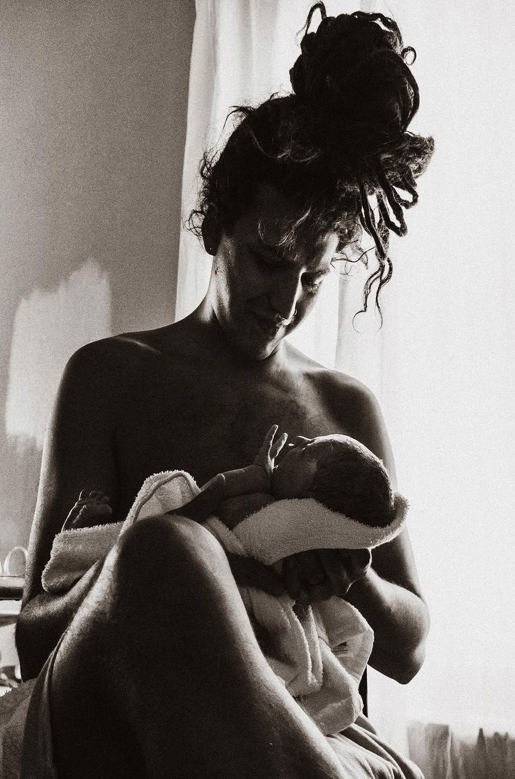 Black and white photo of a mother tenderly cradling her newborn baby by a bright window.