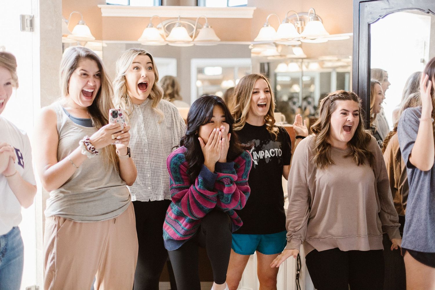 Excited bridesmaids reacting with joy and surprise during wedding preparations at a bridal salon.