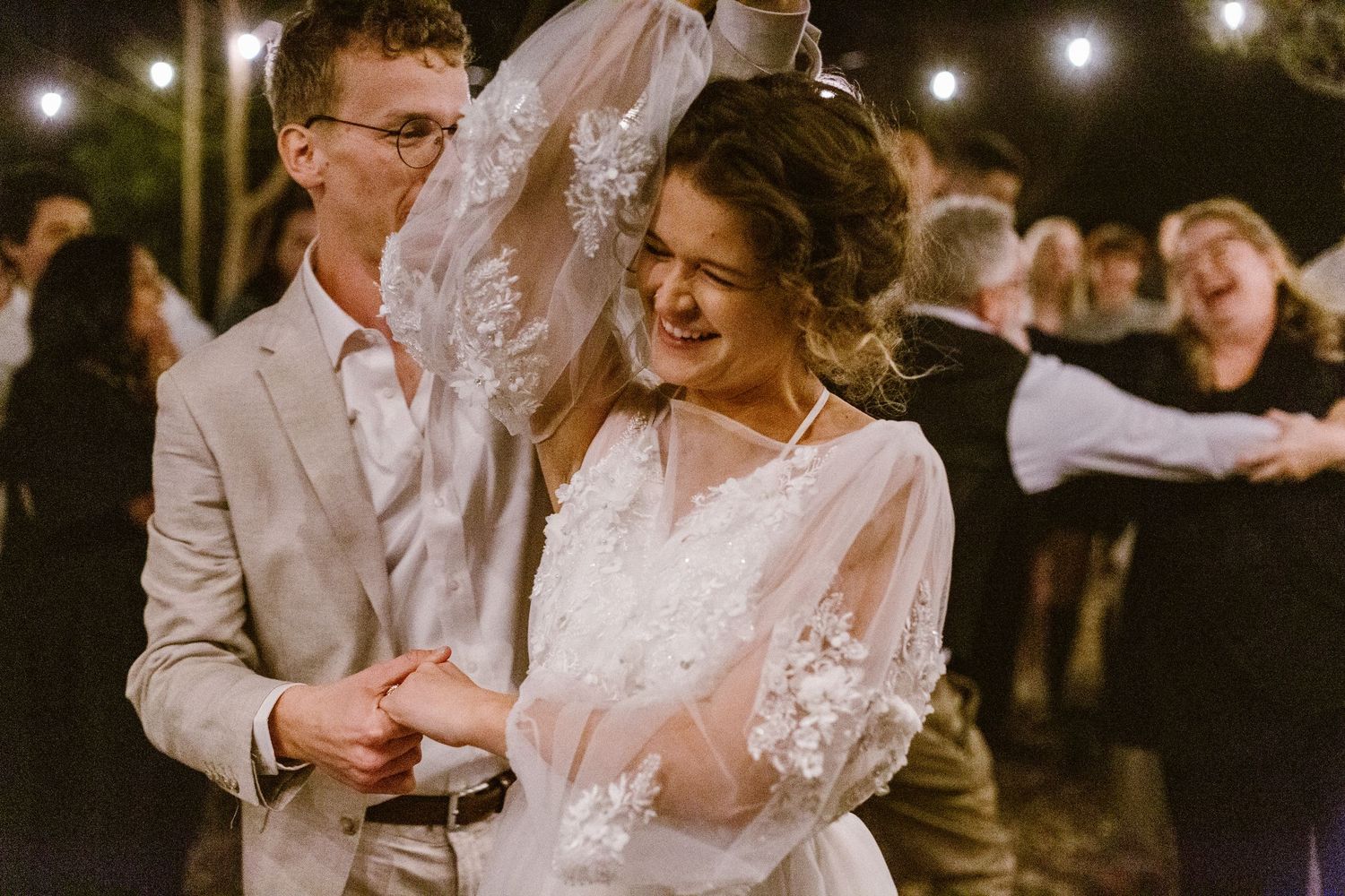 Bride laughing joyfully while dancing with groom at outdoor wedding reception.