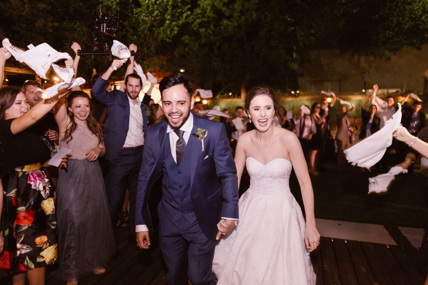 Bride and groom exit wedding celebration as guests wave napkins in joyful send-off.