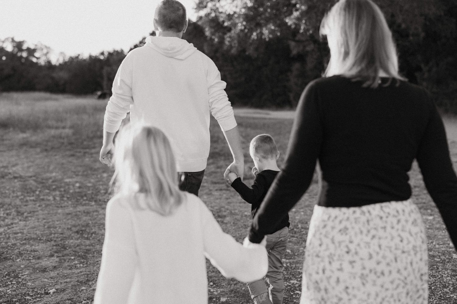 Black and white photo of a family of four walking hand in hand through a field.