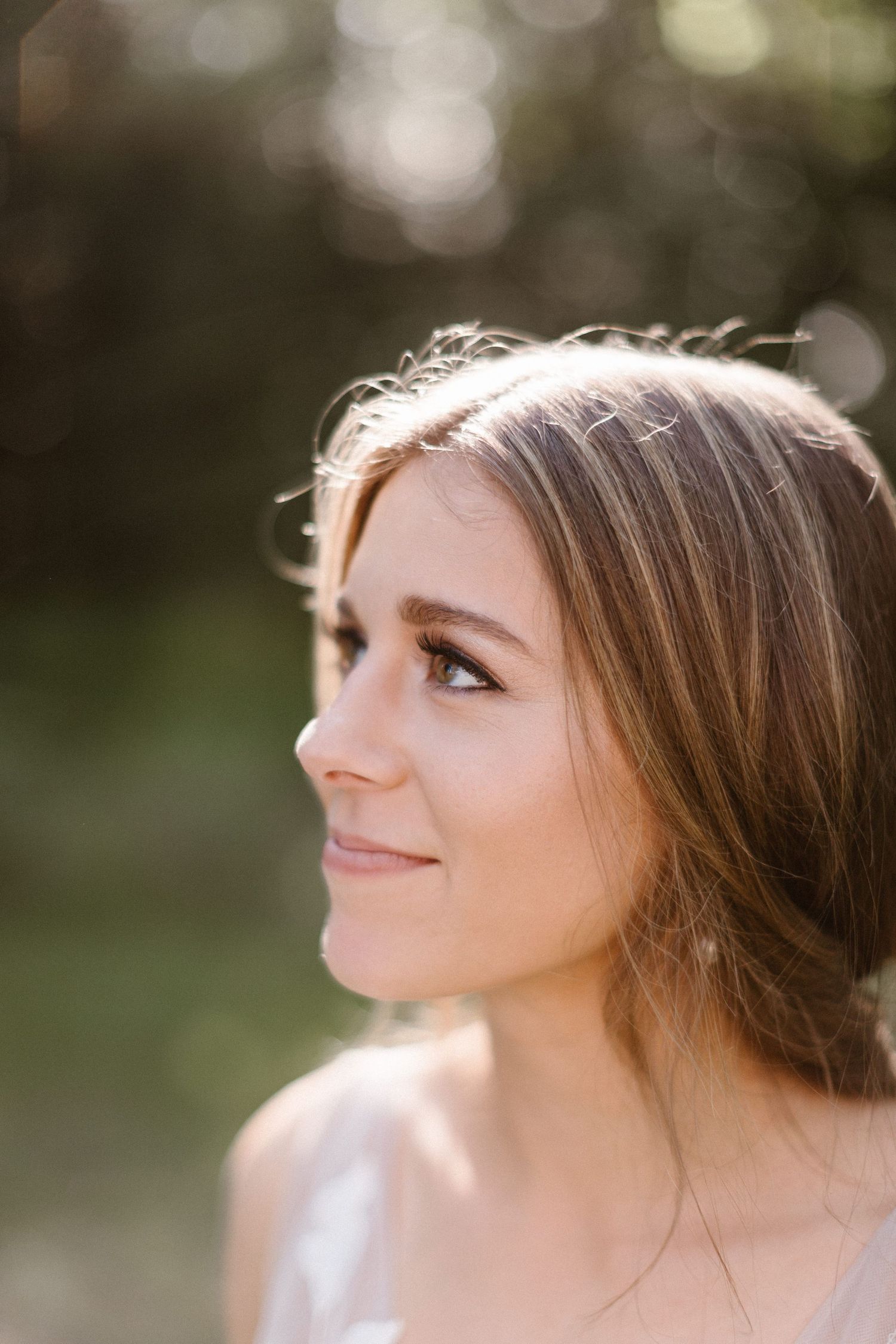 Close-up portrait of a smiling bride with brown hair in soft natural sunlight outdoors.