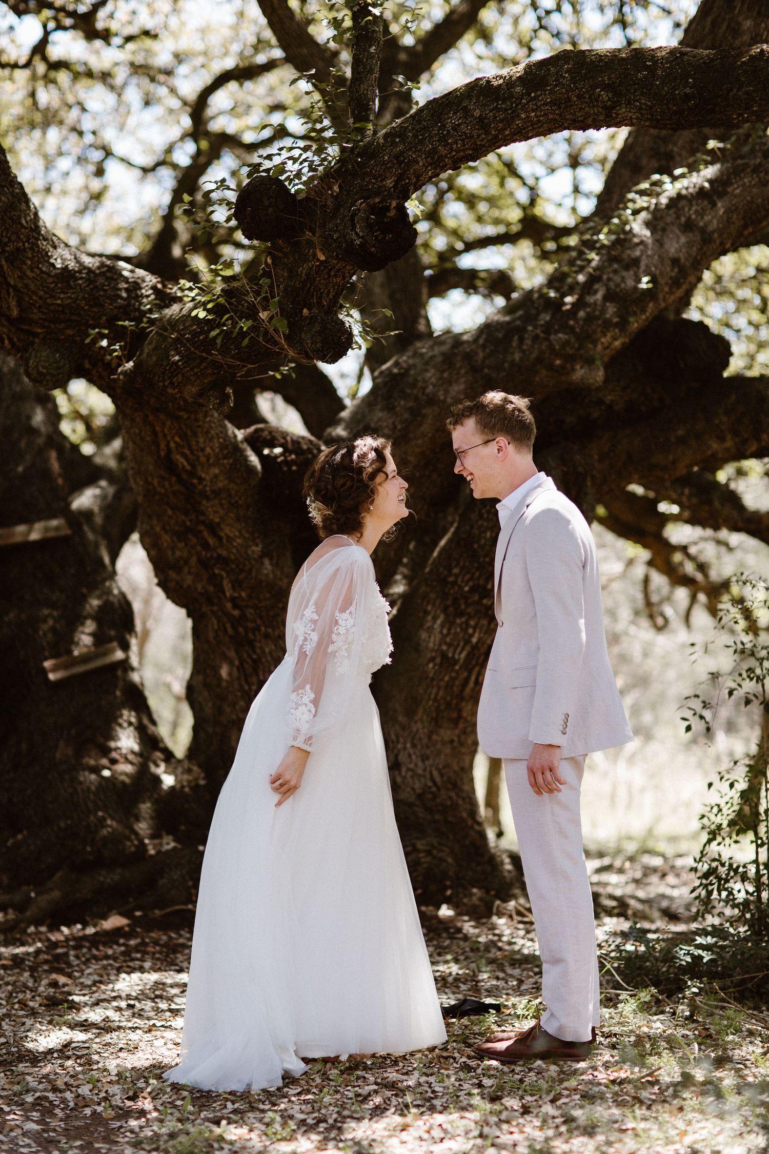 Bride and groom sharing a romantic moment beneath a large oak tree outdoors.
