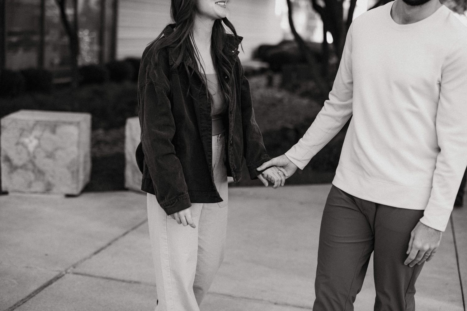 Black and white photo of a couple holding hands walking together on an outdoor sidewalk.