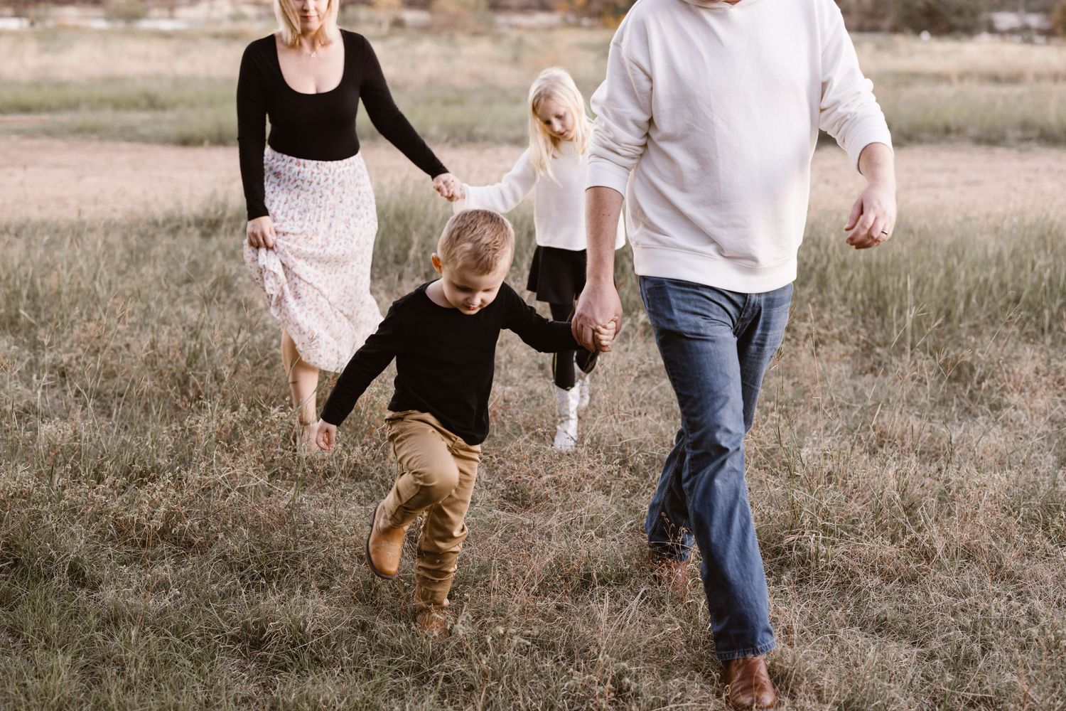 A family of four walking hand-in-hand through an open grassy field at dusk.