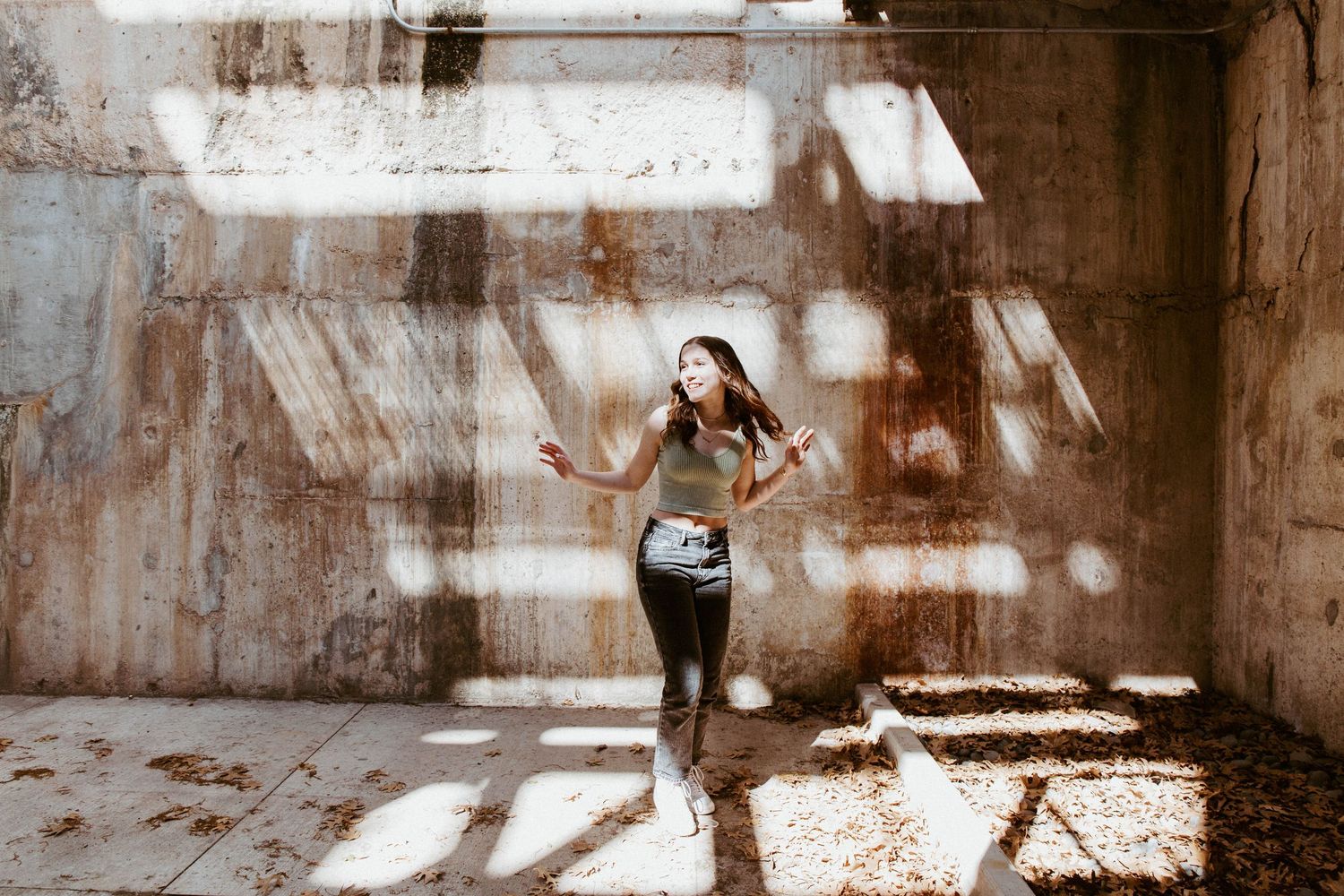 Young woman running through an abandoned industrial building with dramatic sunlight casting shadows on the walls.