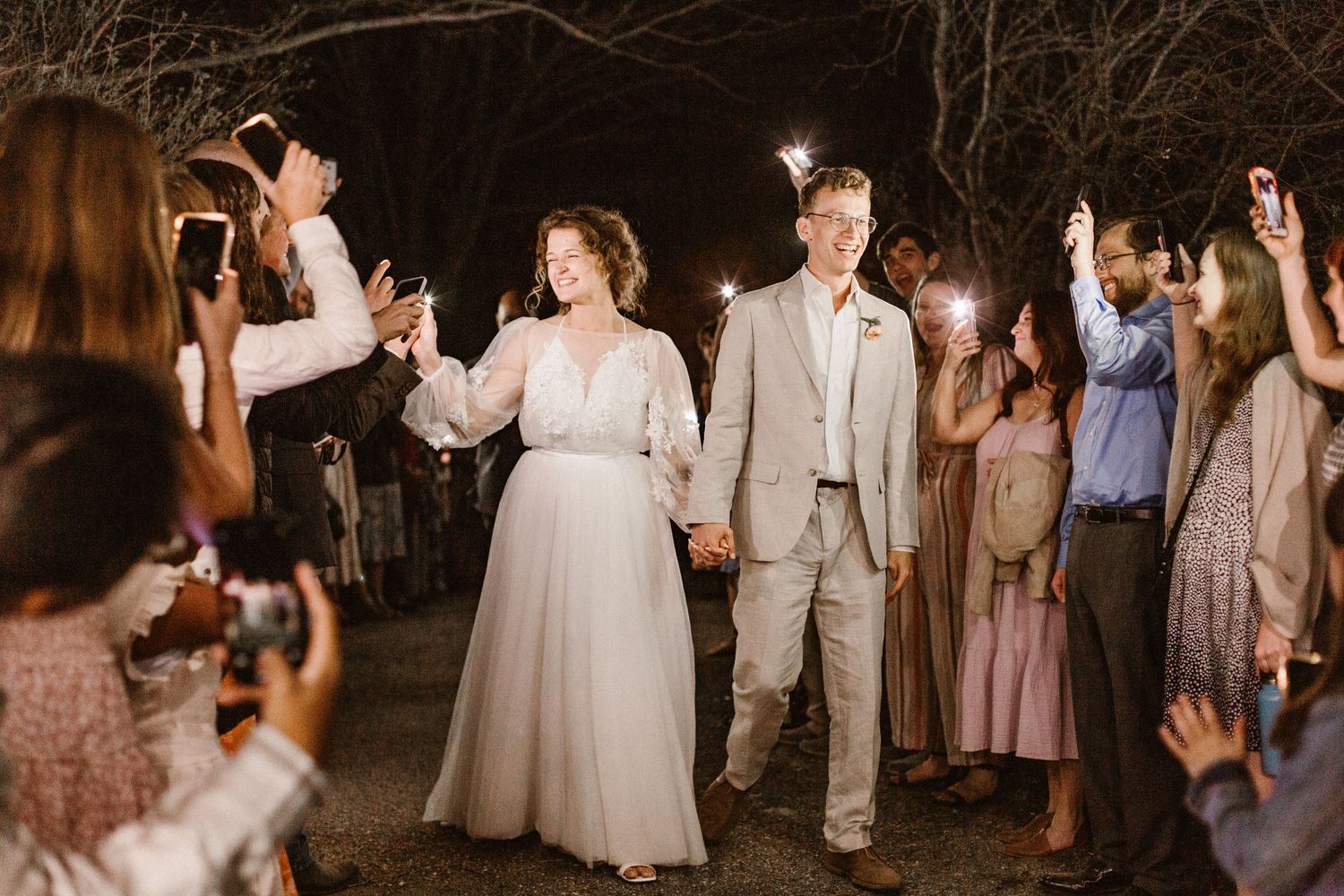 Bride and groom exit wedding reception through sparkler send-off with cheering guests.