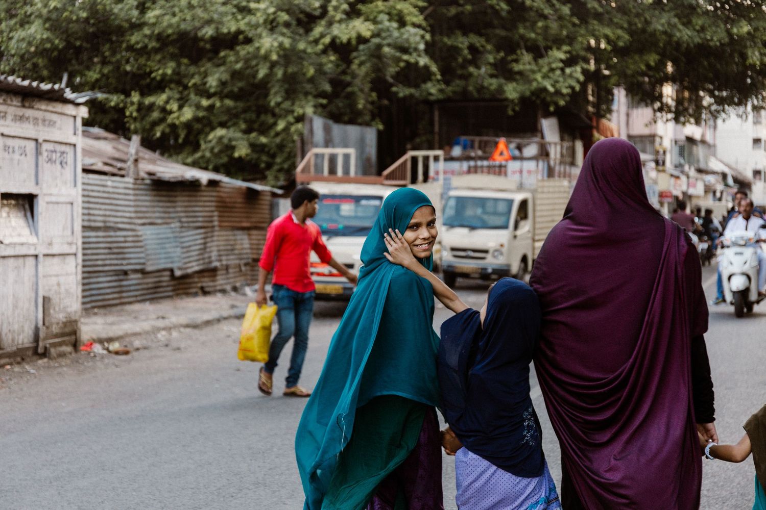 Women in colorful hijabs walking and smiling on a busy urban street in India.