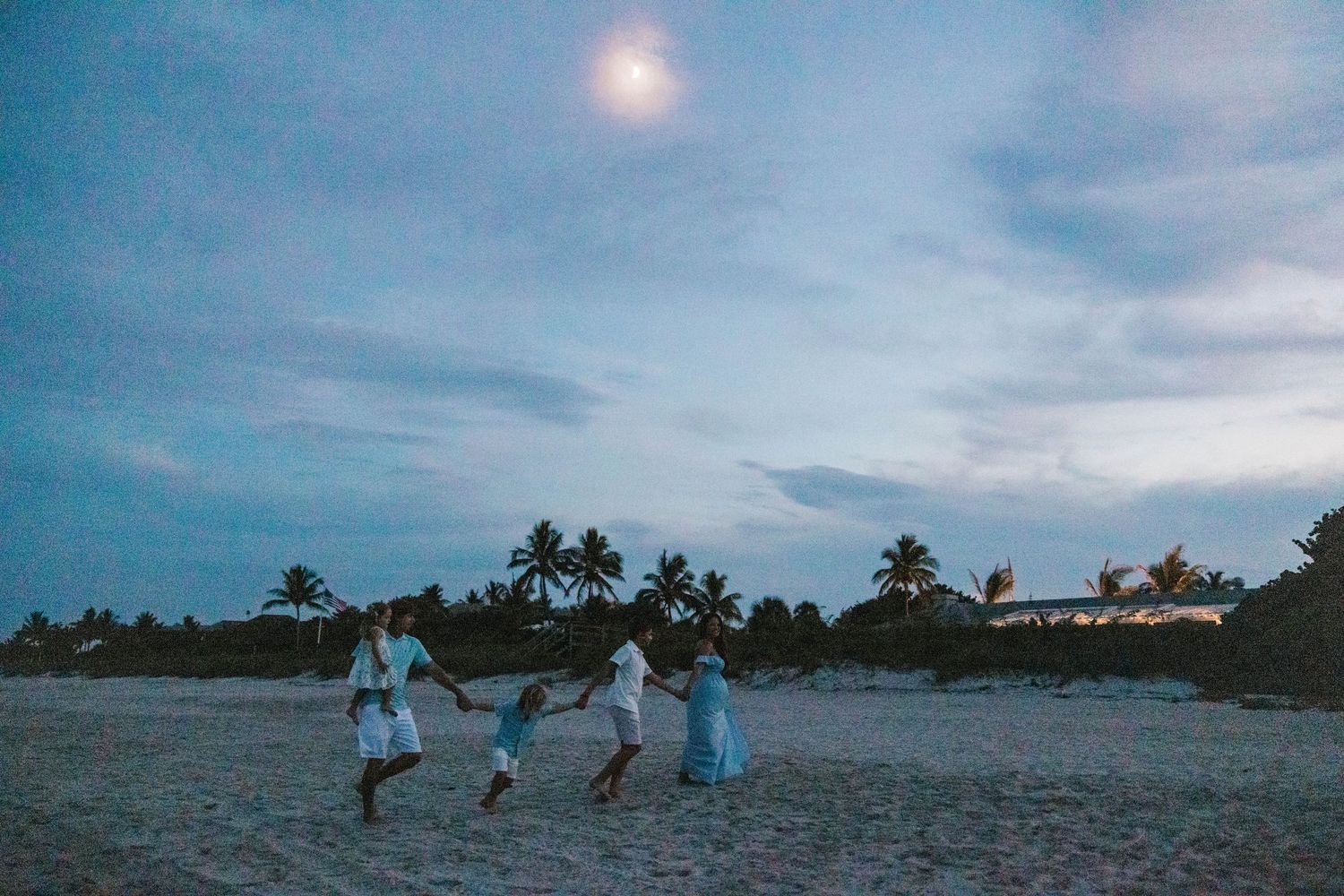A family holding hands and running together on a moonlit tropical beach.