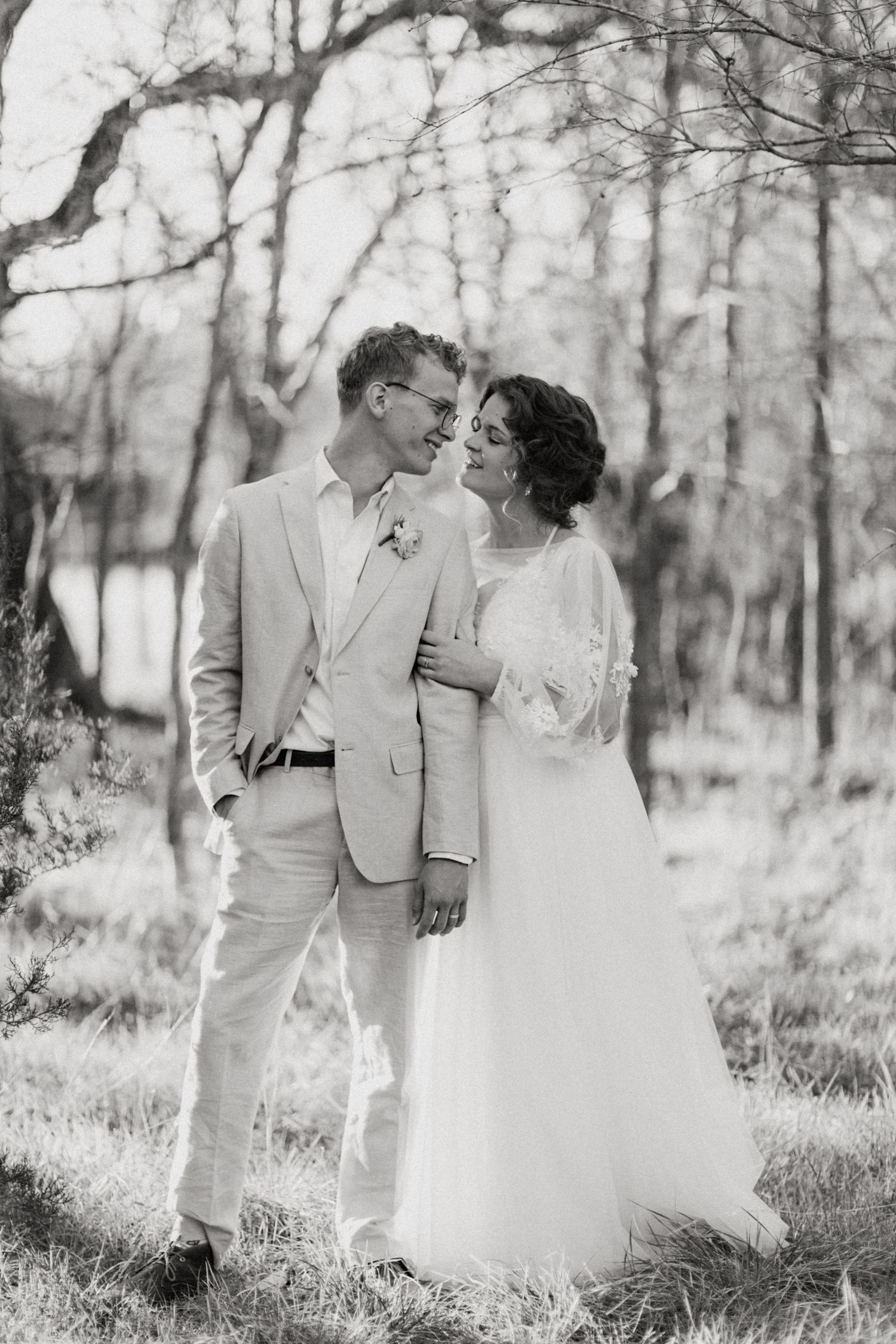 Black and white portrait of bride and groom gazing at each other in sunlit woodland setting.