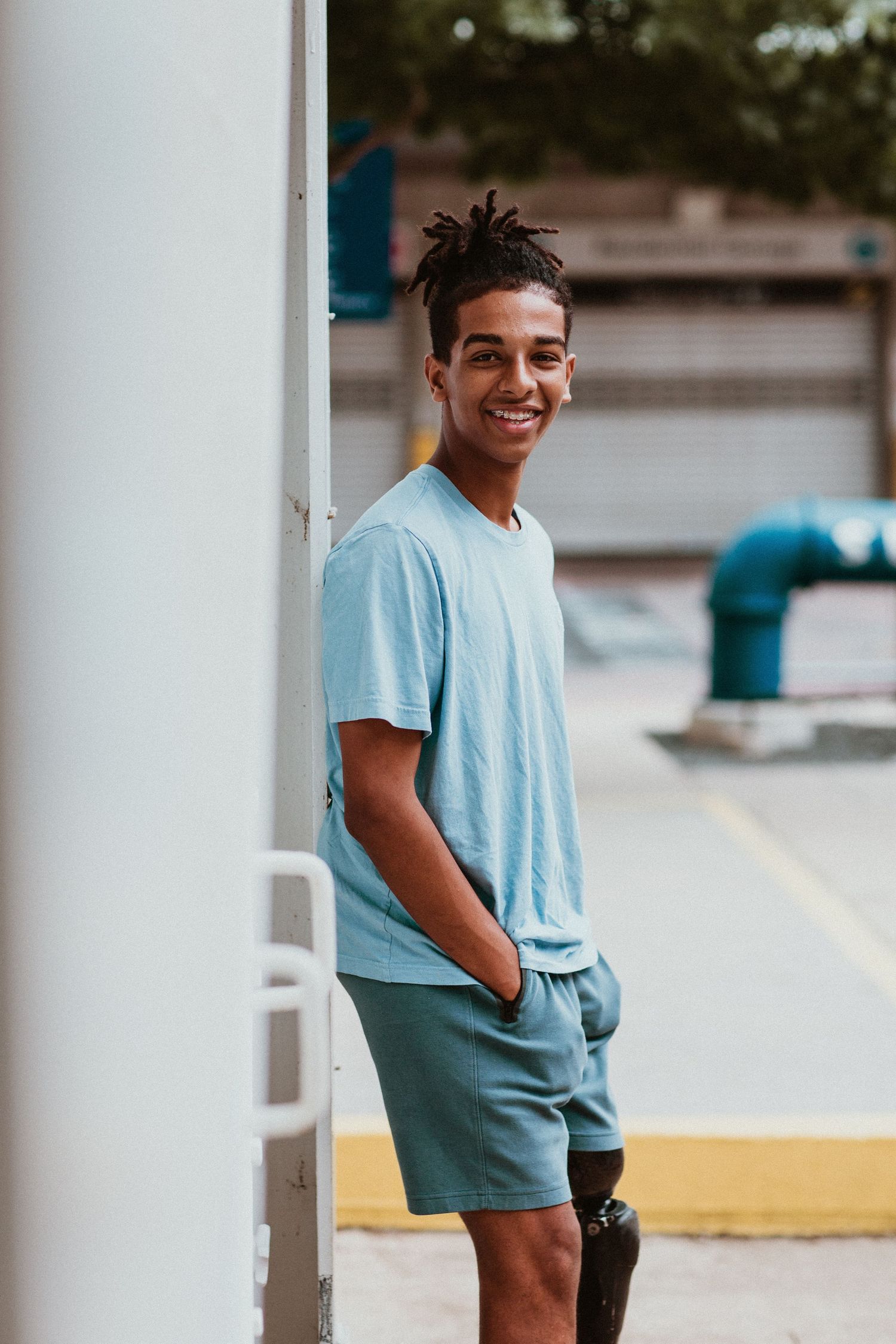 Smiling young man with prosthetic leg leaning against white pillar outdoors.