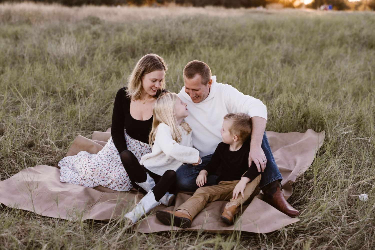 Family of four sitting together on a blanket in a grassy field at golden hour.