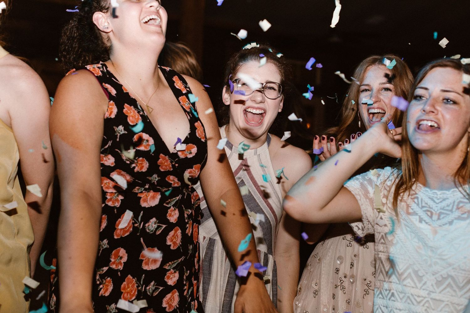 Joyful wedding guests laugh and dance as confetti falls during lively reception celebration.