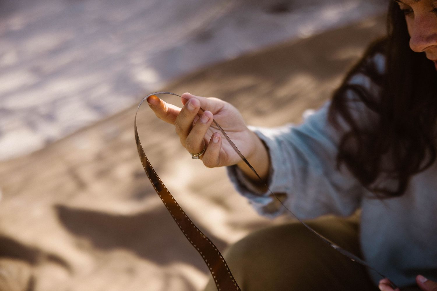 Close-up of hands holding vintage camera film strip on sandy beach in sunlight.