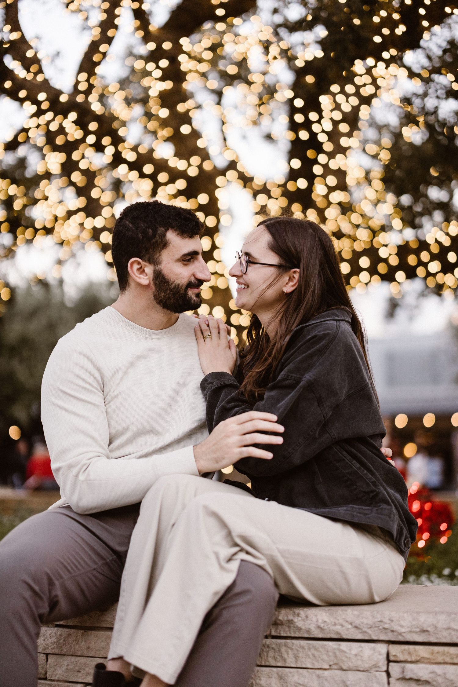 Smiling couple sitting together in front of a tree with warm bokeh lights.