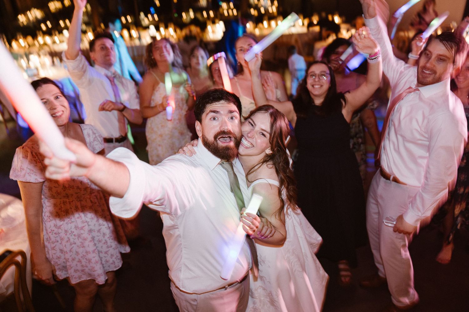 Bride and groom take a fun selfie with glowing guests during lively wedding reception dance party.