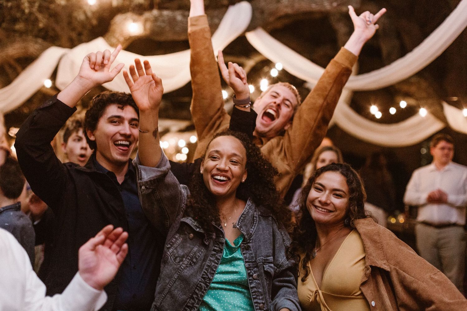 Group of friends cheering and dancing joyfully at an outdoor wedding reception.