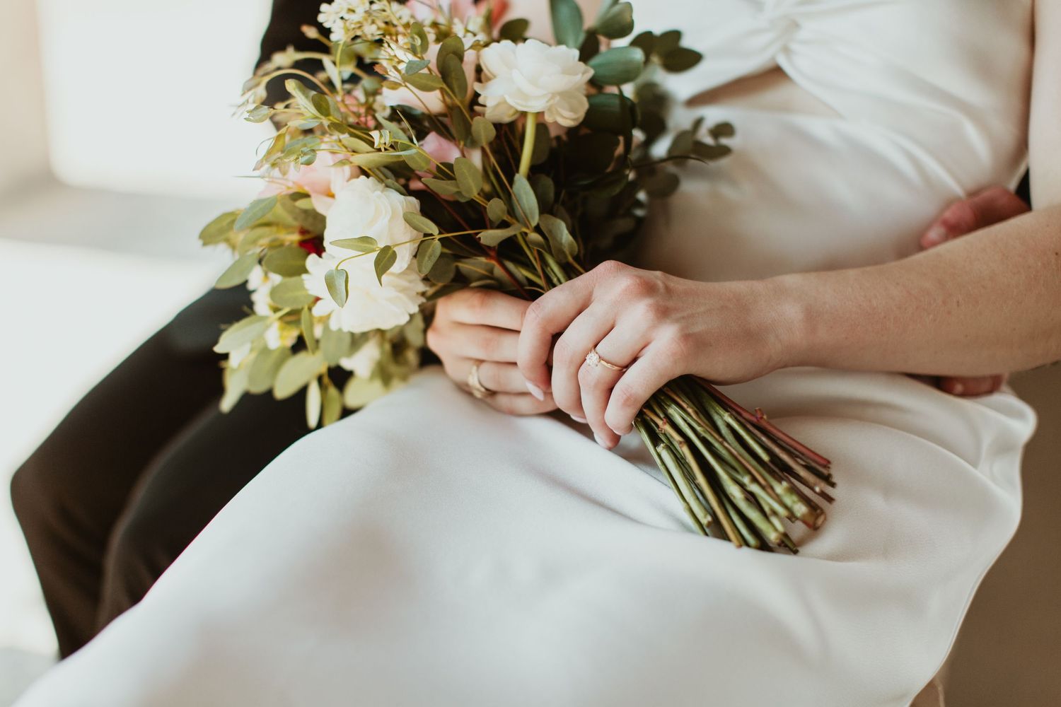 Bride in white dress holding a elegant floral bouquet with roses and greenery on her wedding day.