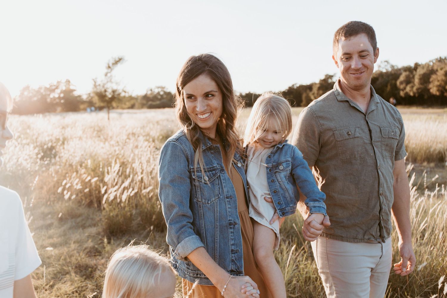 Happy young family with two children walking through a golden sunlit field during sunset.