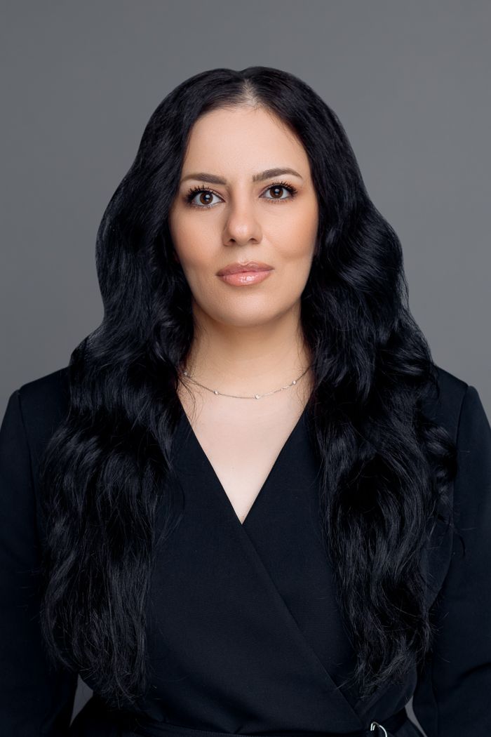 Professional studio portrait against grey background featuring long black hair and black v-neck top.