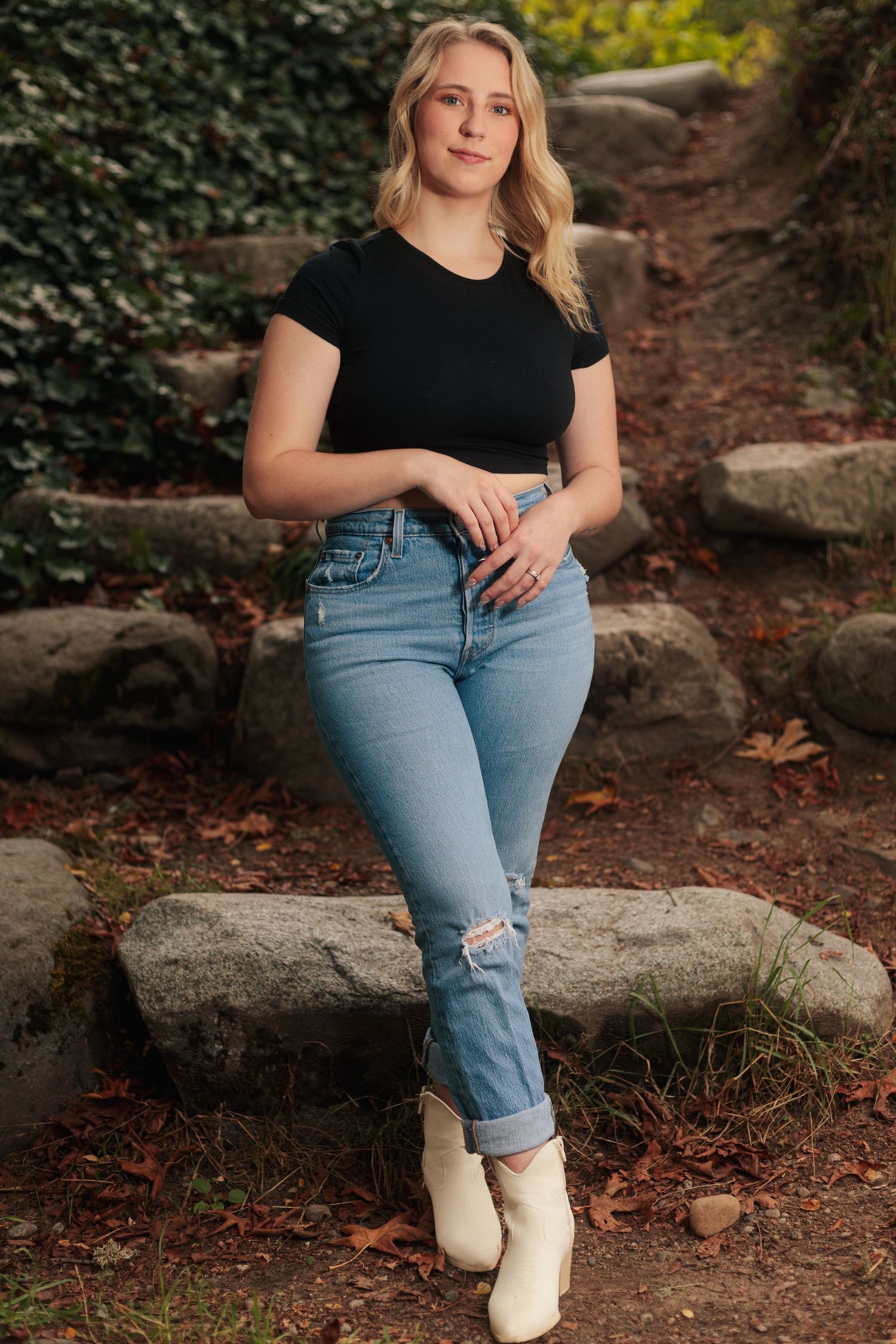 Casual outdoor photoshoot featuring jeans, black top and white boots against a natural rocky backdrop.