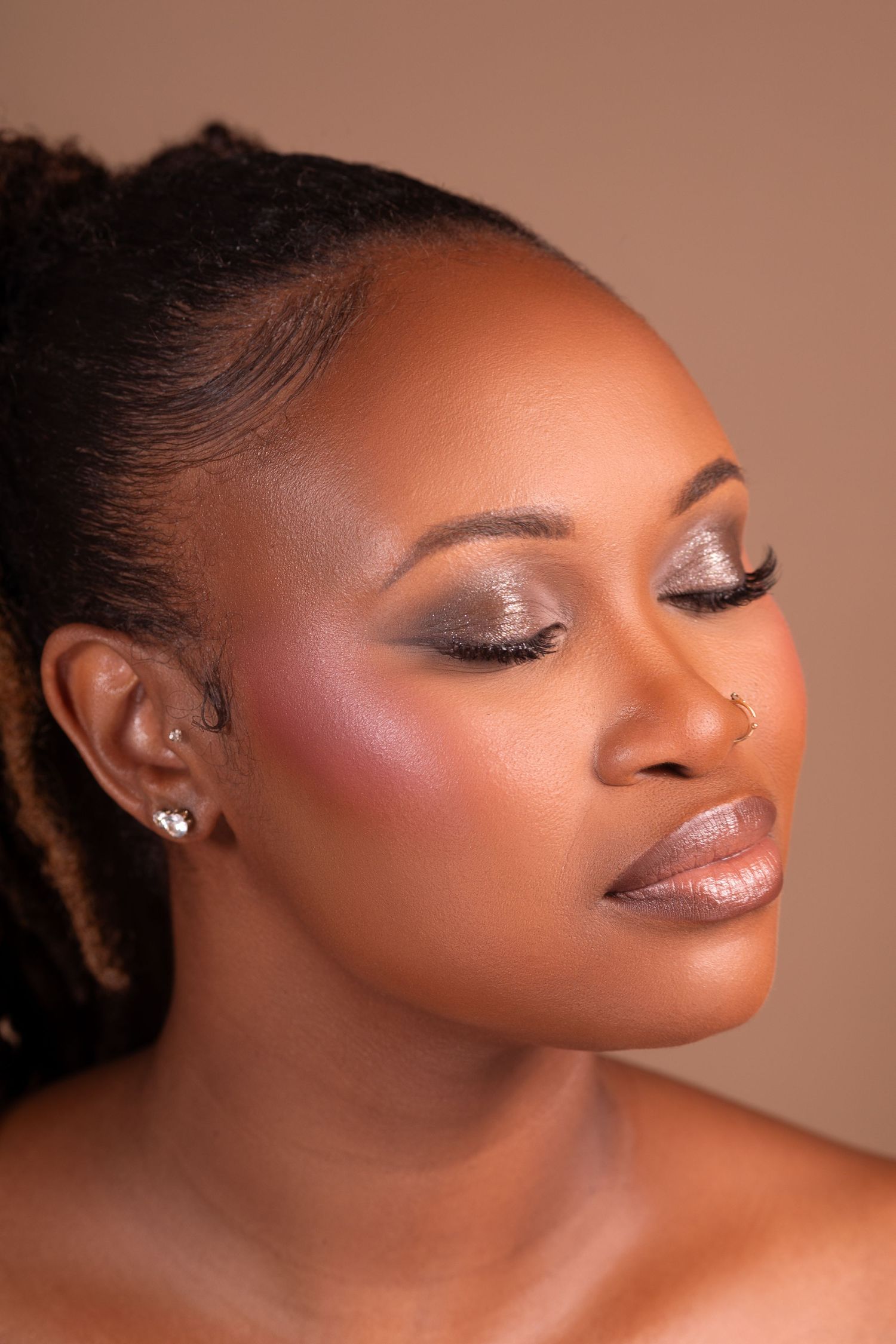 Close-up portrait of a Black woman with glam makeup, shimmery eyeshadow, and locs, eyes closed, neutral background.