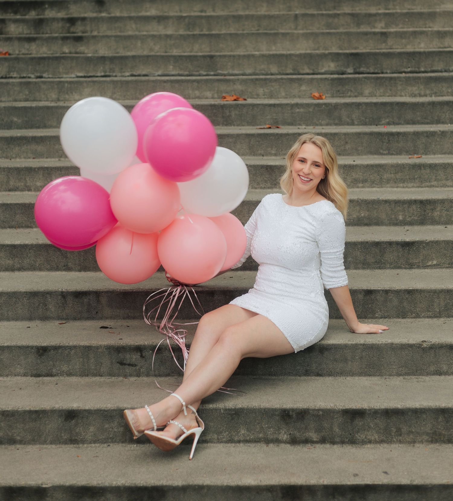 White dress and pink balloons create a playful scene on concrete steps.