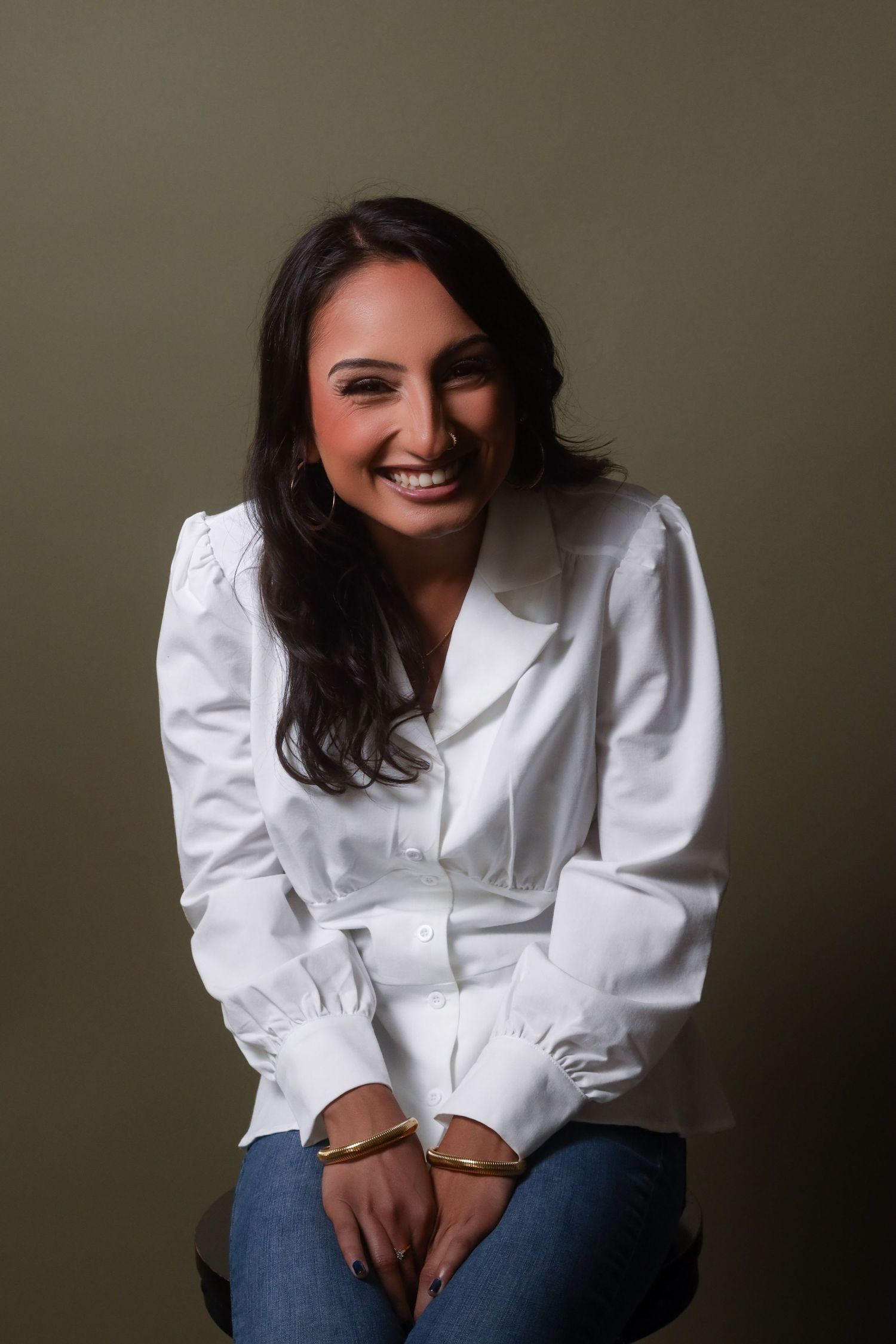 Person in white button-down shirt and jeans poses casually against grey background.