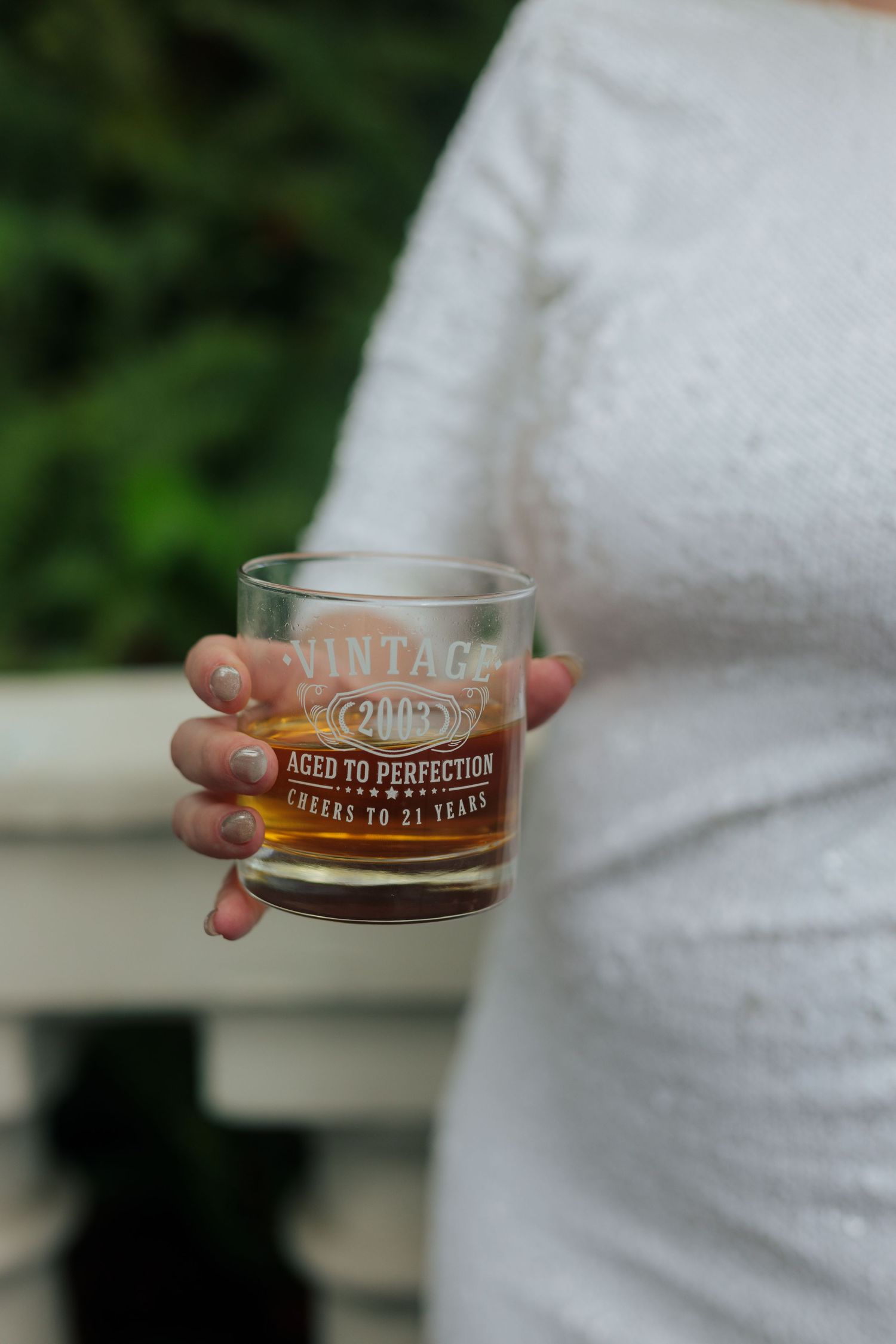 Close-up shot of a hand holding a whiskey glass with text 'Aged to Perfection' visible.