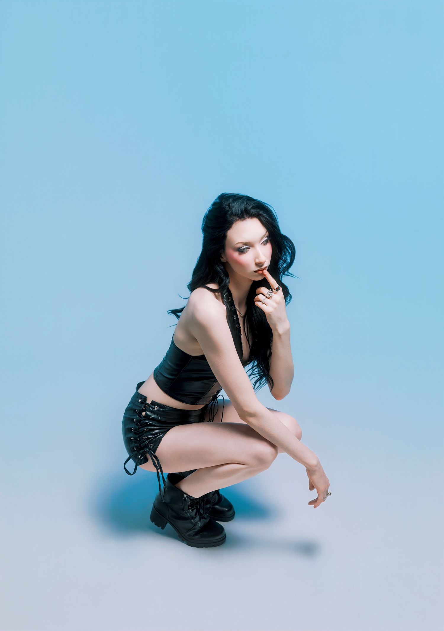 Young woman in black crop top and shorts crouching against a light blue gradient background.
