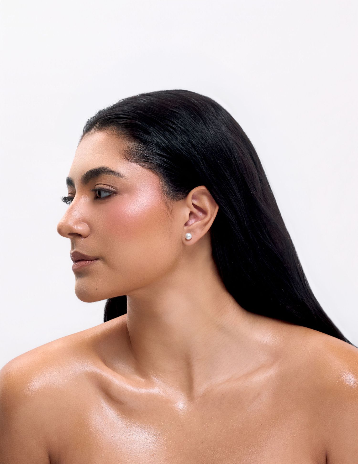 Woman in profile view wearing elegant pearl stud earrings, showcasing minimalist jewelry against a white background.