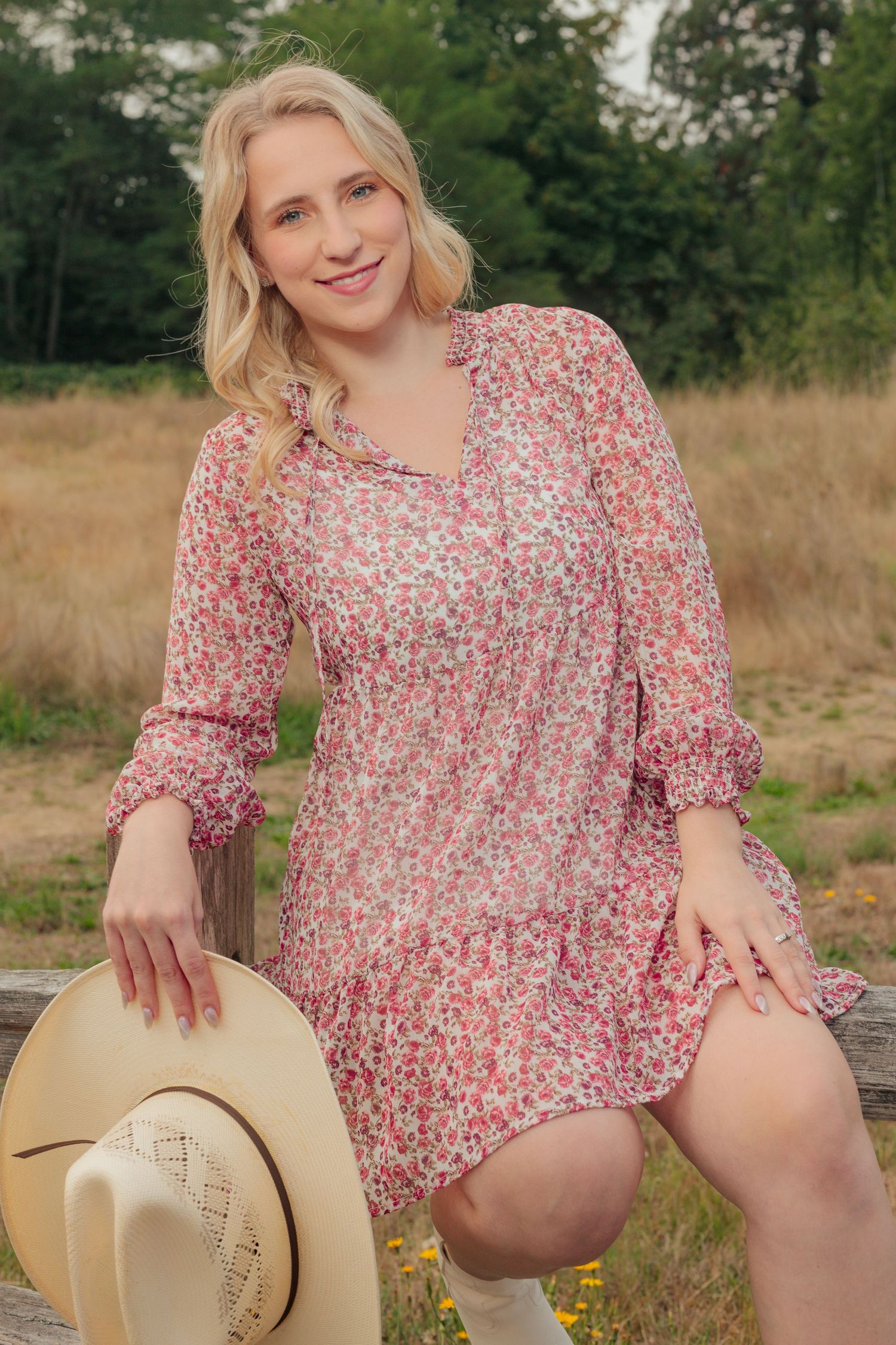 Person in a pink floral dress poses with a beige cowboy hat in a grassy field.