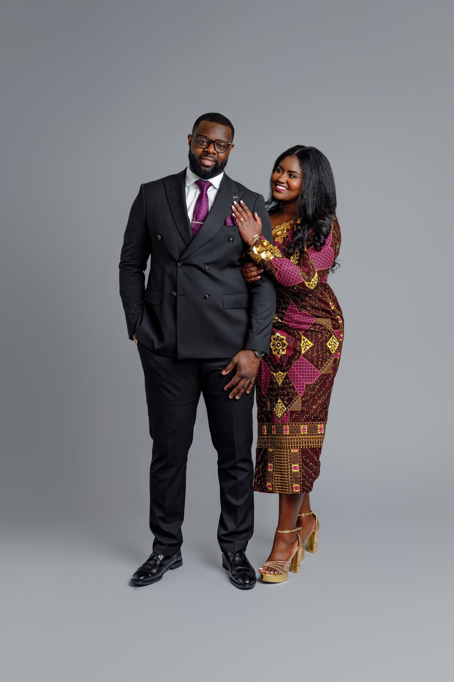 Stylish couple posing together, man in black double-breasted suit, woman in colorful African print dress.