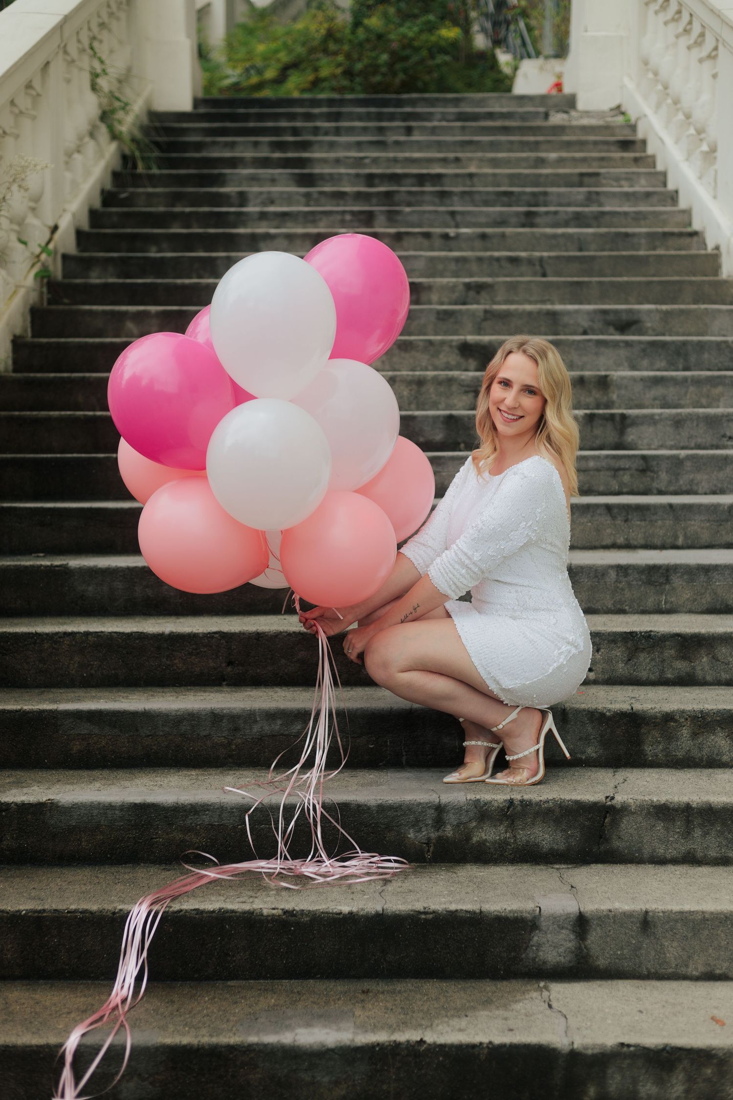 Romantic photoshoot featuring pink and white balloons on grand stone staircase.