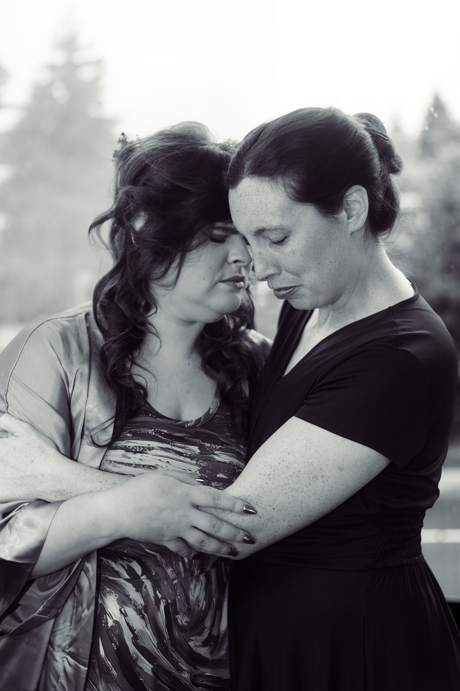Black and white intimate portrait of two people sharing a tender moment outdoors.