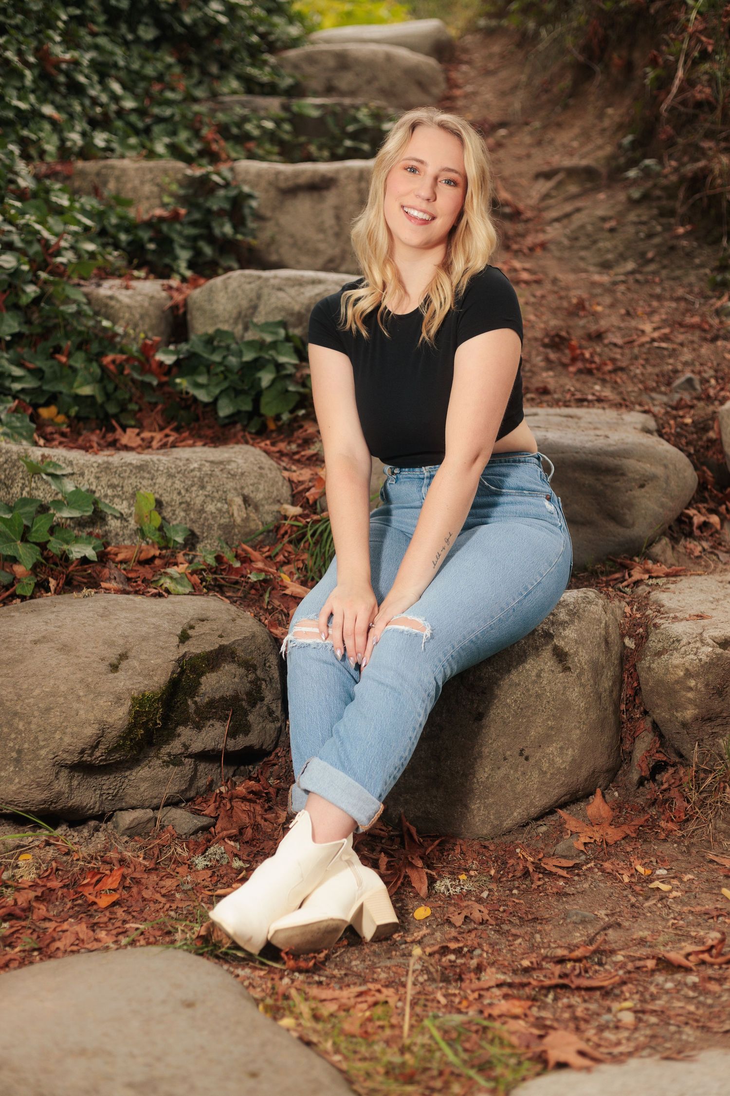 Person in casual attire sitting on rocky terrain surrounded by fallen leaves.
