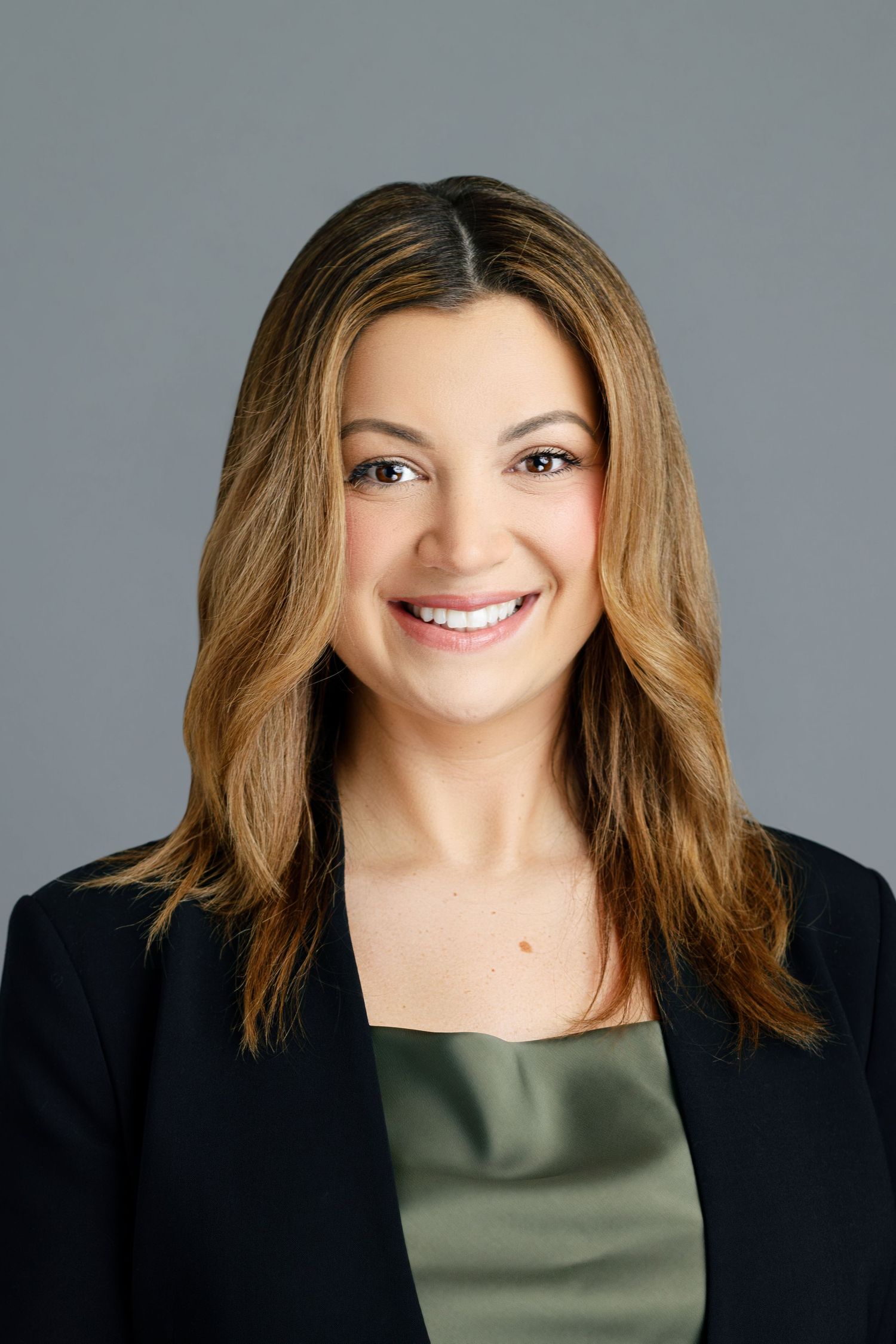 Professional headshot of a smiling woman with brown hair wearing a black blazer and olive green top.