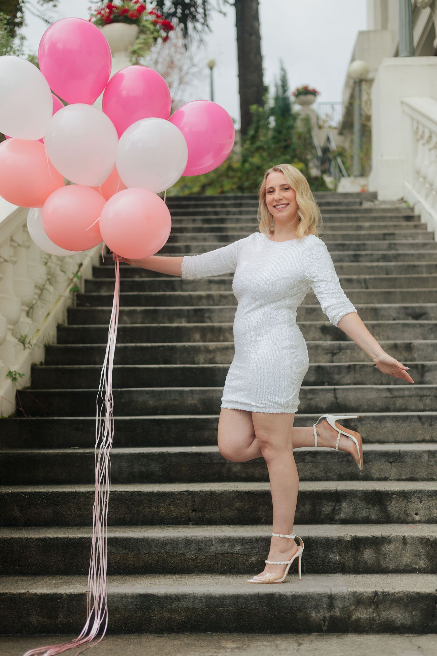 Pink and white balloons accent a grand stone staircase in an elegant outdoor photoshoot.