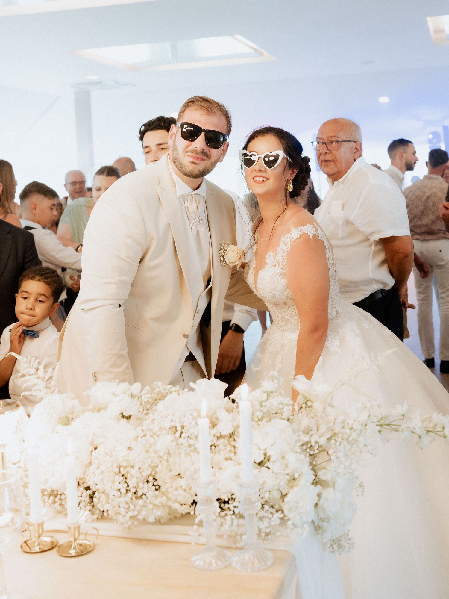 Noivos de óculos escuros posam em uma elegante recepção de casamento toda branca, com arranjos florais na Quinta de santo Andre