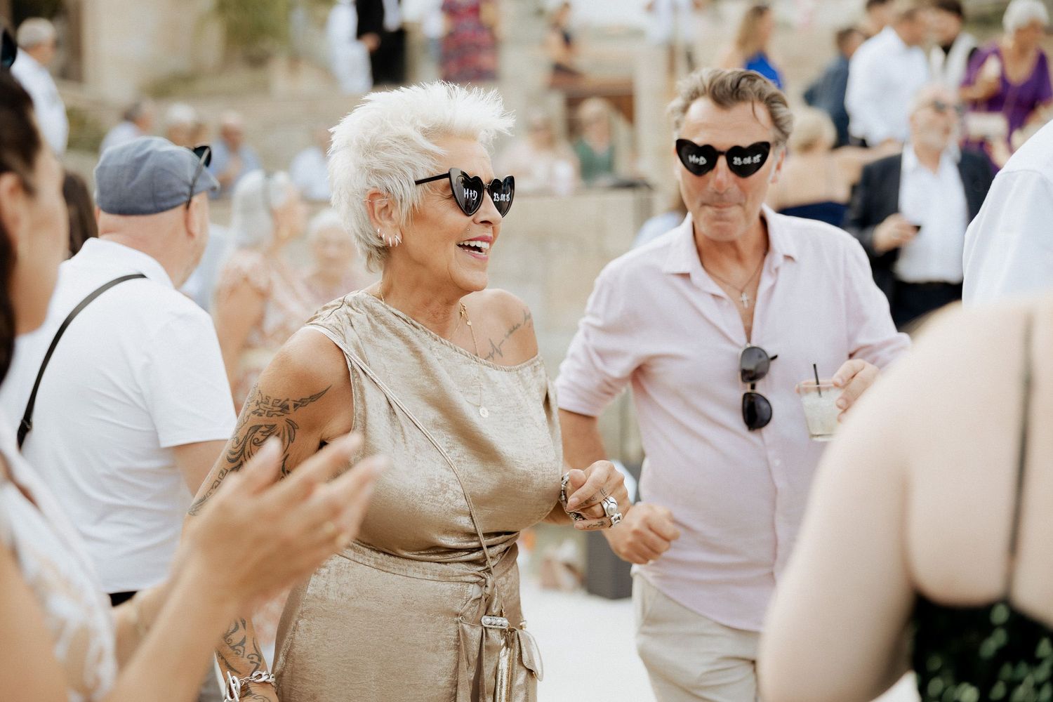 Mulher mais velha elegante, vestindo um vestido dourado e óculos de sol, socializando  em uma sofisticada festa na Quinta da Pia.