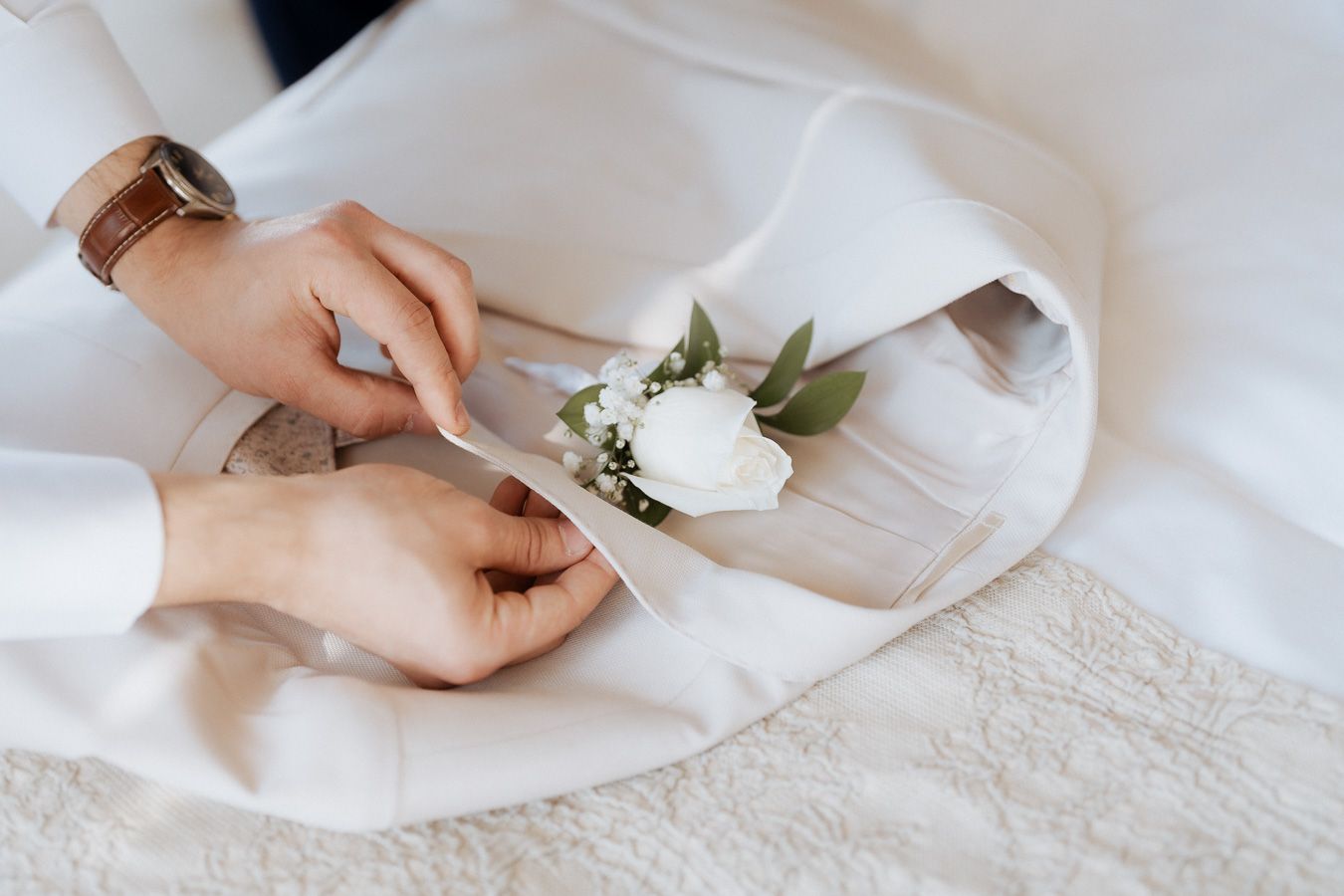 Detalhe de mãos prendendo uma rosa branca na lapela de um terno de casamento. casamento na Quinta do Carvalho em Viana do Castelo