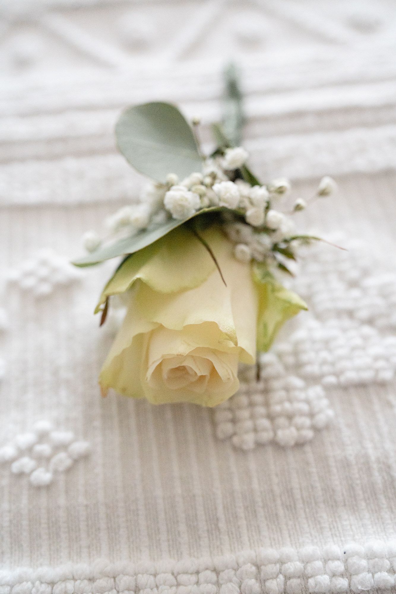 Elegante Rosa Branca de lapela com eucalipto sobre tecido de renda marfim. Casamento na Quinta da Pia, Barcelos
