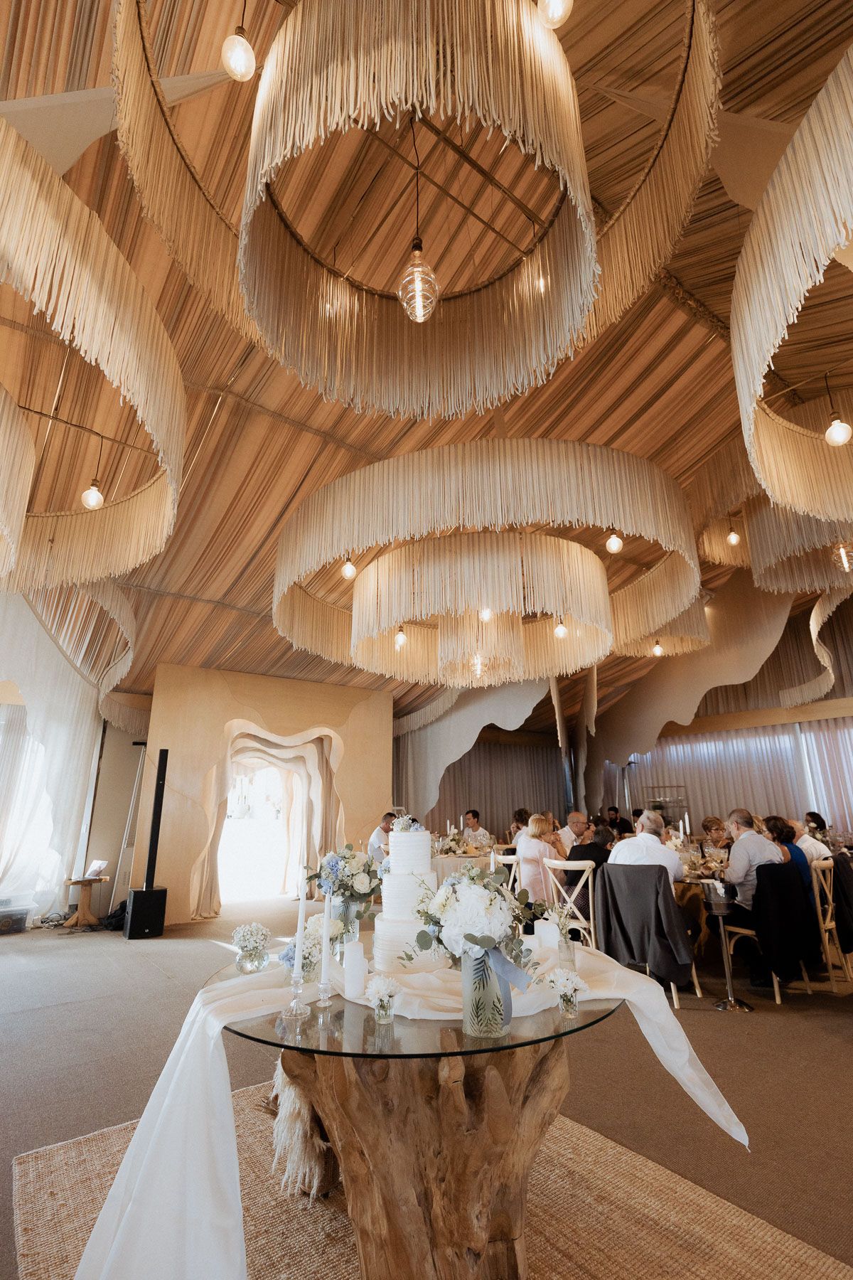 Elegante salão de recepção de casamento com deslumbrantes lustres de franjas, mesa rústica feita de tronco de árvore e convidados jantando s