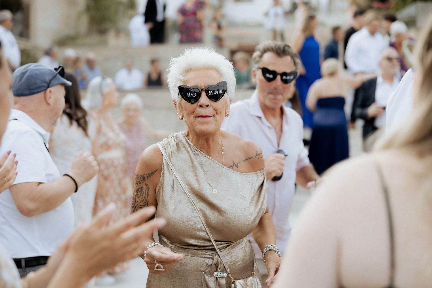 Idosa de óculos escuros e vestido dourado dançando em uma confraternização ao ar livre ou recepção de casamento na Quinta da Pia Barcelos