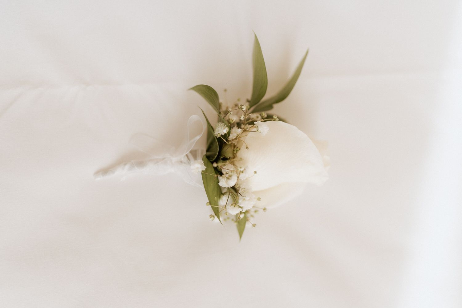 Elegante flor de lapela em forma de rosa branca com folhagens e gipsofila sobre um fundo de tecido branco suave. quinta do Carvalho