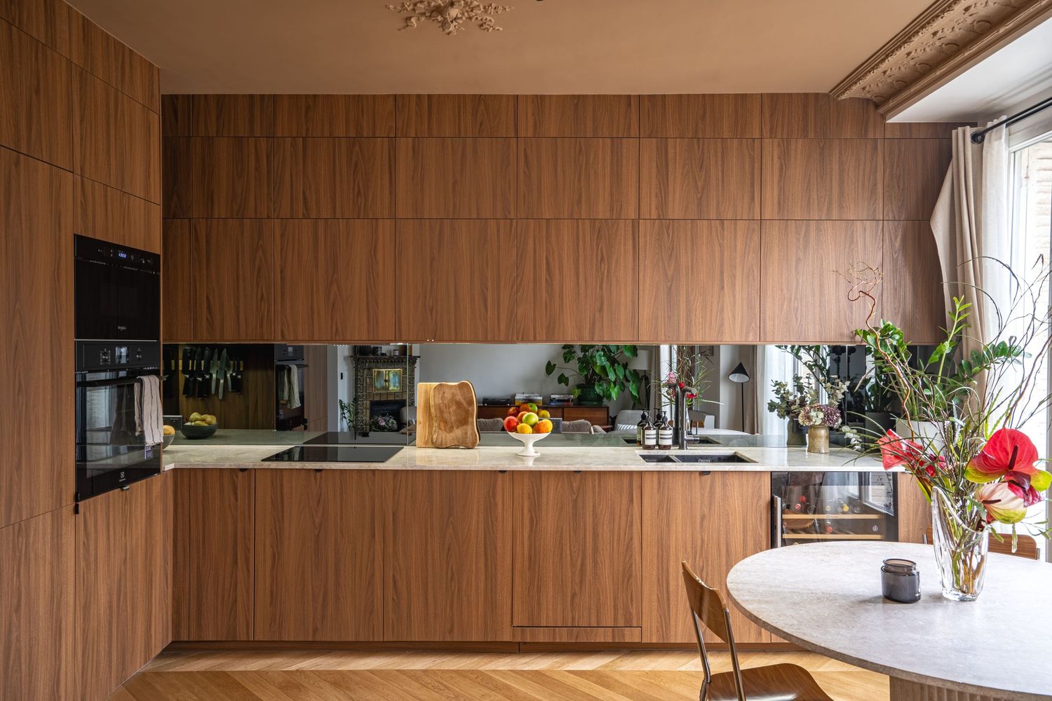 Modern kitchen with warm walnut wood cabinetry, mirrored backsplash, marble countertops, and herringbone parquet flooring.