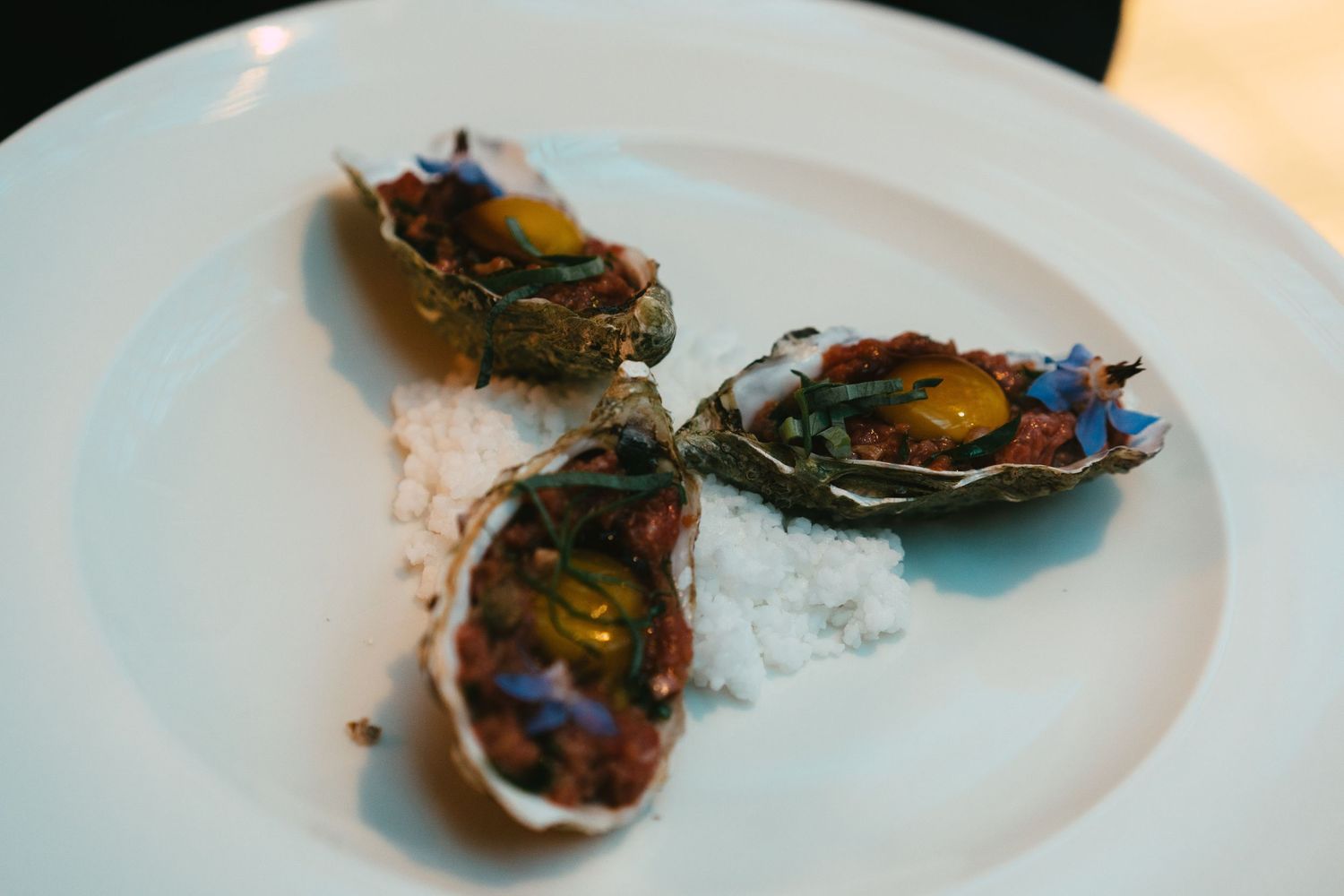 Three fresh oysters garnished with edible flowers served on a white plate with salt.