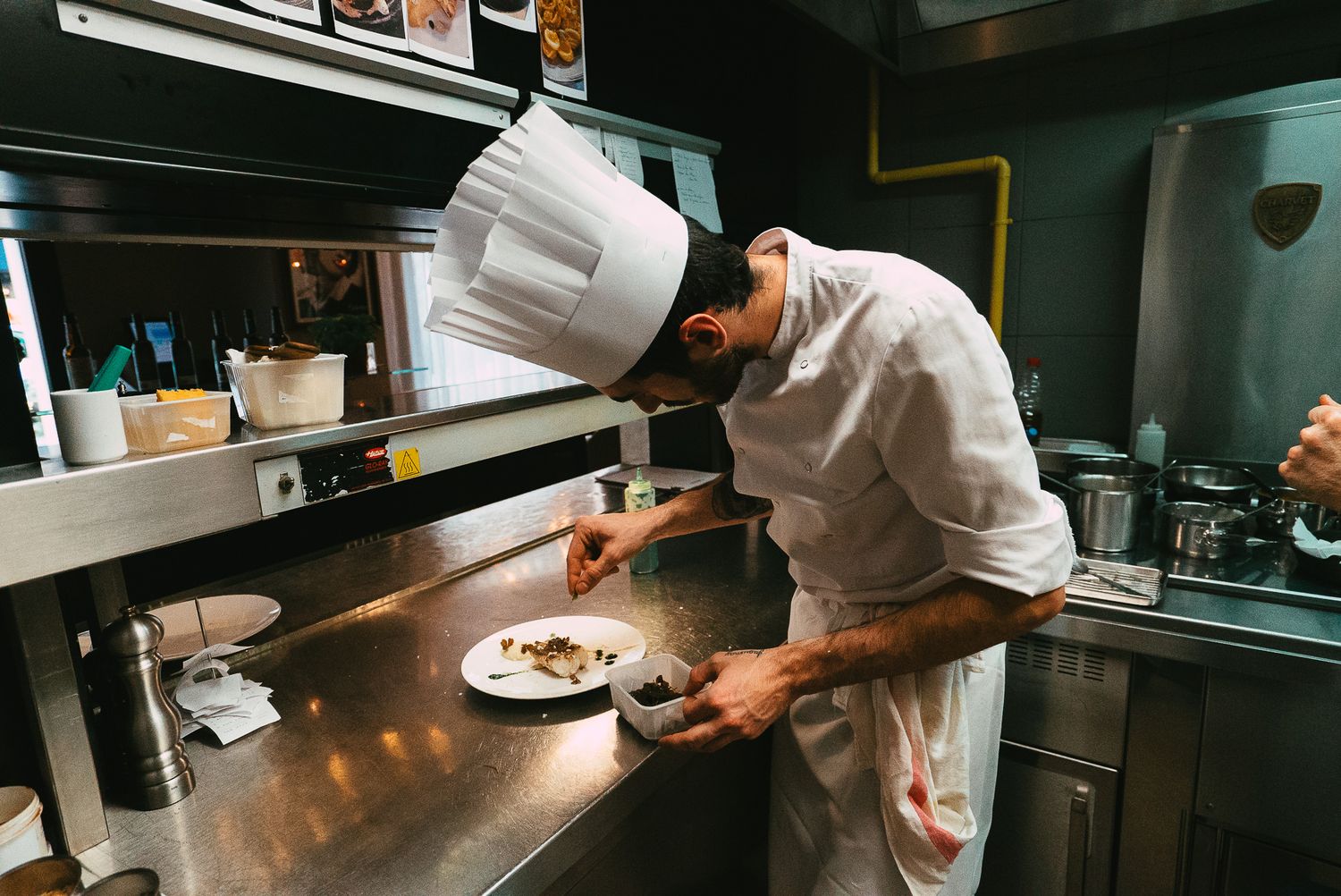 Professional chef in white uniform carefully plating a gourmet dish in a restaurant kitchen.