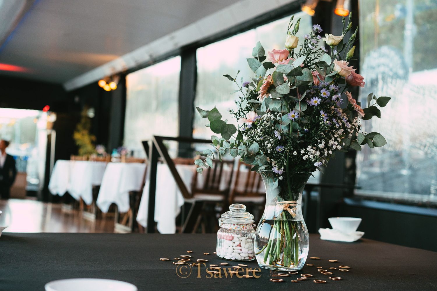 Lush floral centerpiece with eucalyptus and roses on a dark table in a riverside reception venue.
